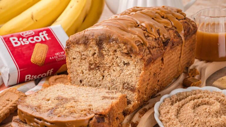 Sliced Biscoff banana bread showing cookie butter ribbons through the crumb and a Biscoff spread topping, with bananas and a pack of Biscoff cookies behind it by Tessie's Table.