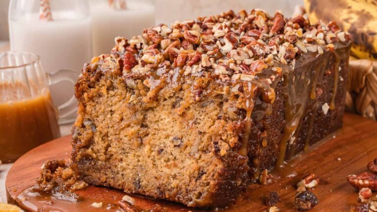Sliced caramel pecan banana bread showing a soft crumb, caramel drips and chopped pecans on top with a jug of caramel sauce by Tessie's Table.