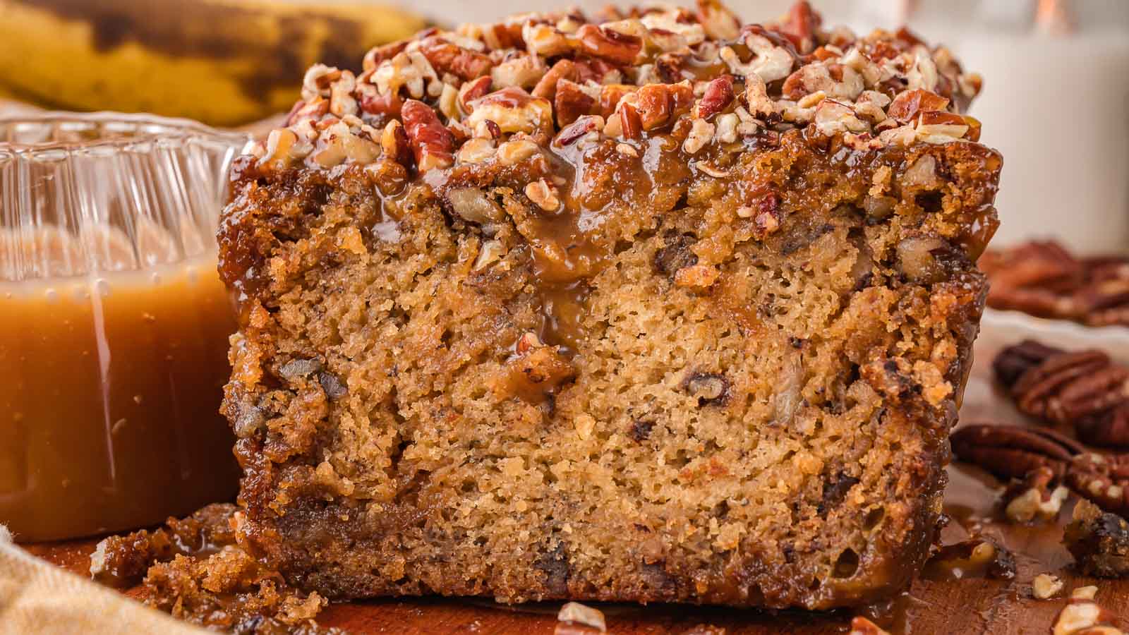 Close up of the cut end of a caramel pecan banana bread loaf showing a soft crumb with pecans and a caramel pecan topping by Tessie's Table.