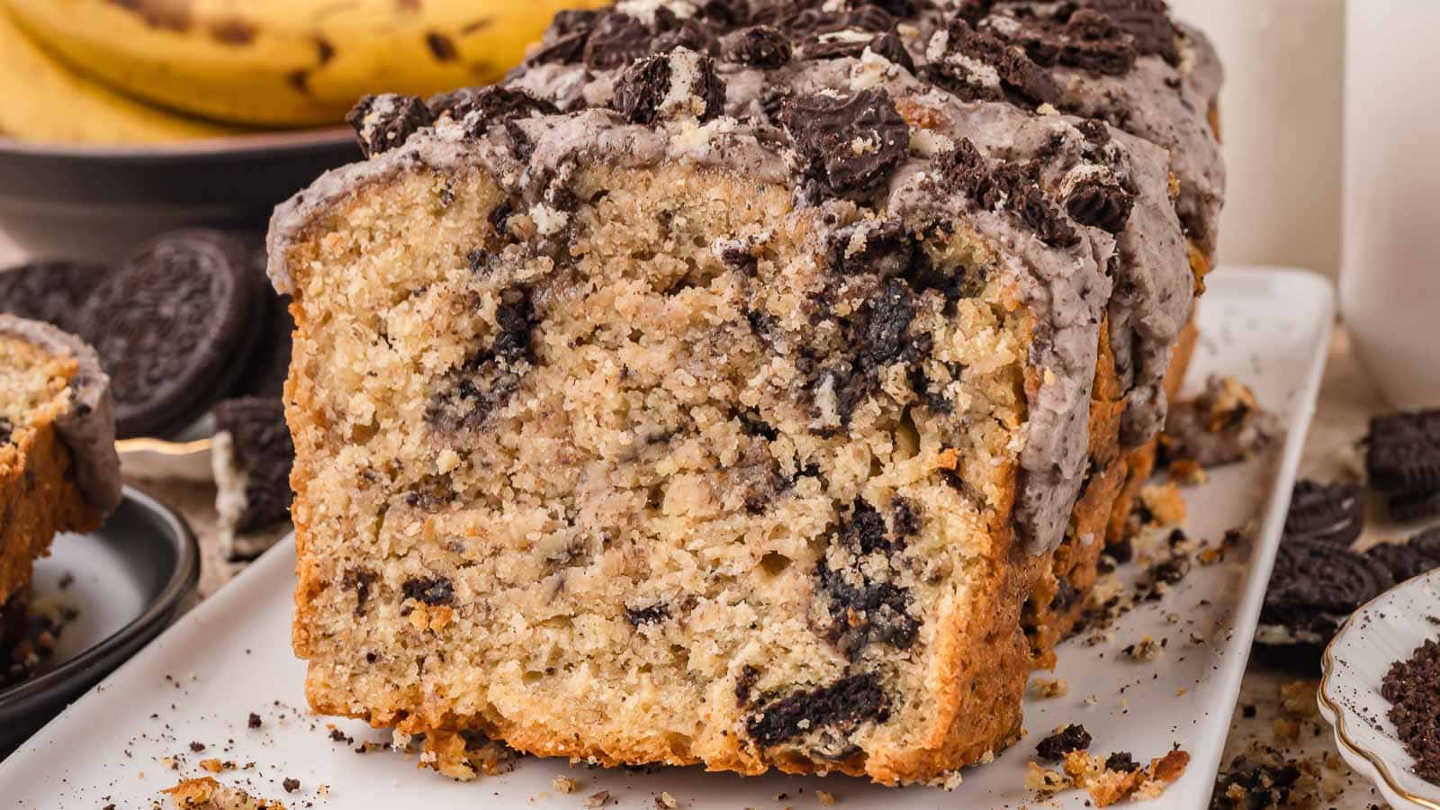 Cut Oreo banana bread loaf showing chopped Oreos through a soft crumb with a cookies and cream glaze and Oreo pieces on top by Tessie's Table.
