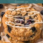 Stack of blueberry crumble cookies with crumble topping and a white chocolate drizzle next to a bottle of milk by Tessie's Table.