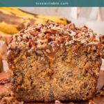 Sliced caramel pecan banana bread with a pecan and caramel topping, with ripe bananas in the background.
