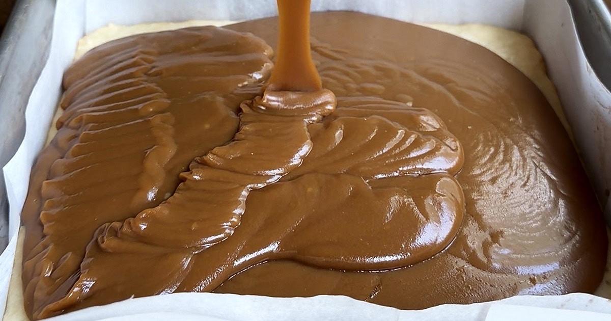 Homemade caramel with sweetened condensed milk being poured over a shortbread base in a lined baking pan by Tessie's Table.