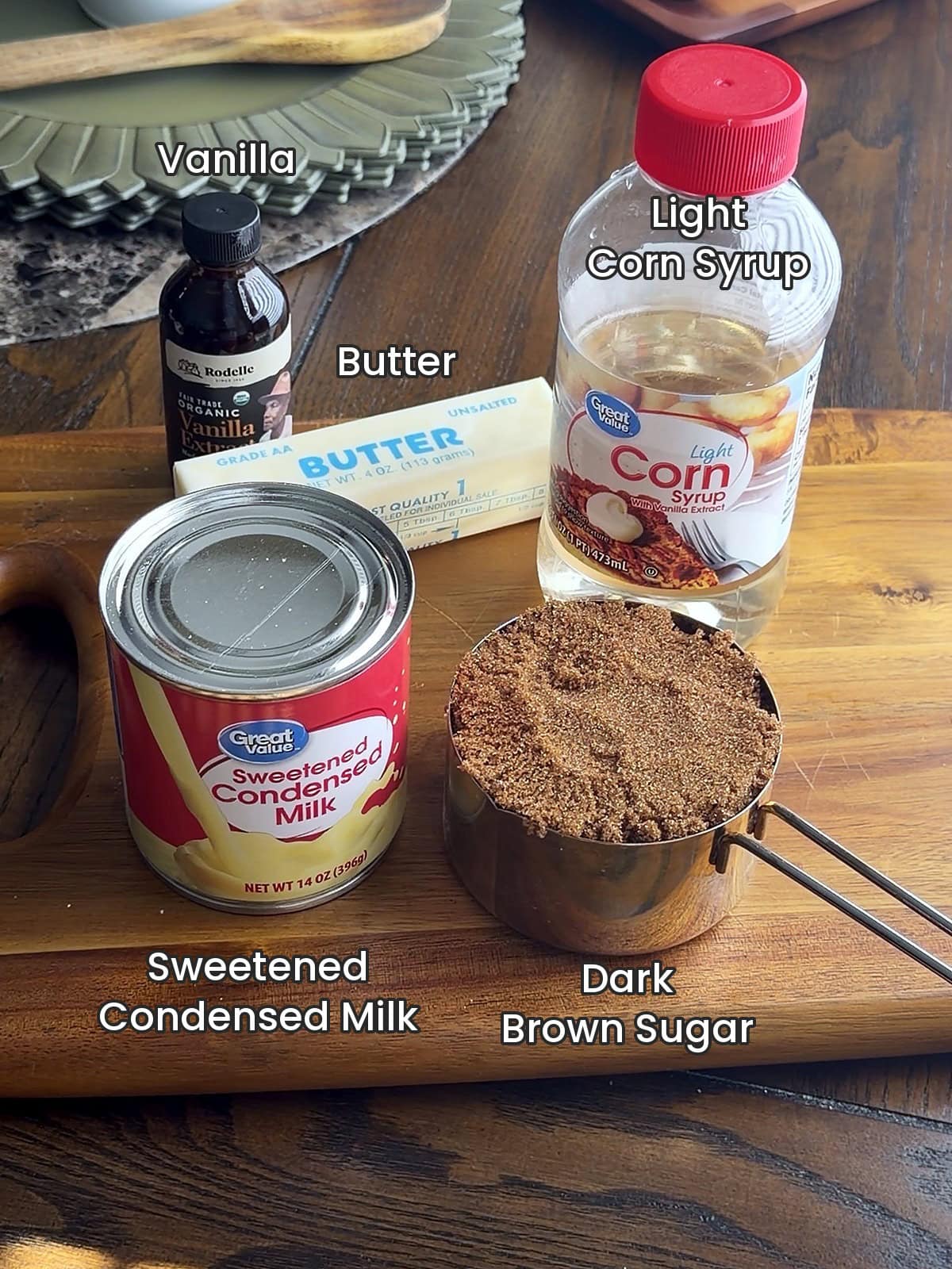Labeled ingredients for caramel with sweetened condensed milk including vanilla, butter, light corn syrup, a can of sweetened condensed milk and dark brown sugar by Tessie's Table.