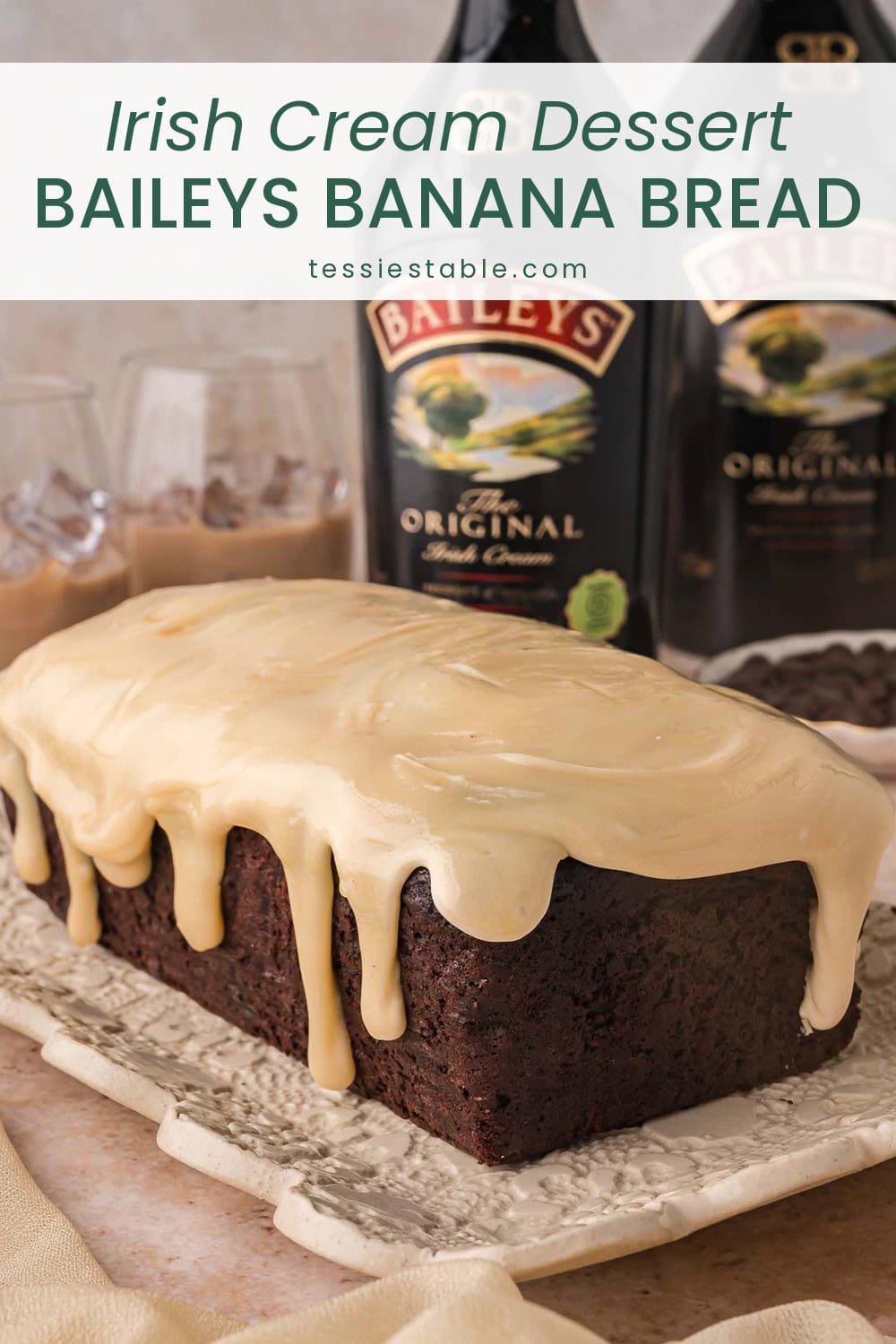 Chocolate Baileys banana bread with white chocolate Baileys ganache dripping down the sides, with Baileys Irish Cream bottles behind it.