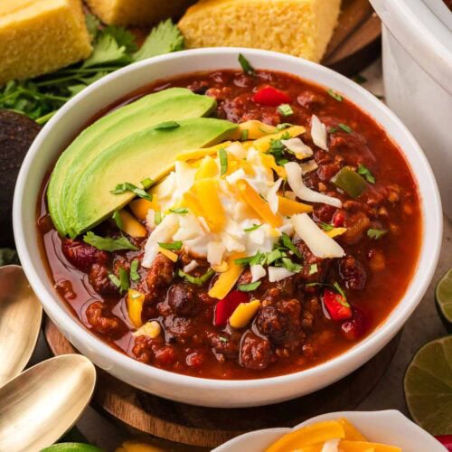 Bowl of slow cooker turkey chili with beans topped with sliced avocado, sour cream, shredded cheese and cilantro by Tessie's Table.